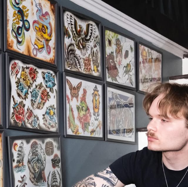Gabe Barker seated in front of a wall of tattoo flash